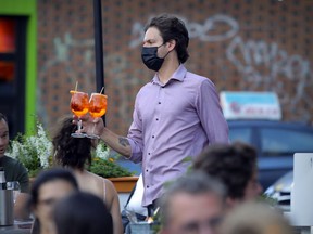 A masked waiter serves drinks at a terrasse on Mount Royal Ave. in Montreal on Aug. 24, 2021.