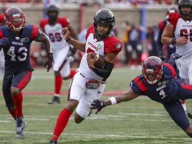 Ottawa Redblacks quarterback Caleb Evans runs between Montreal Alouettes Ahmad Thomas, left, and Monshadrik Hunter during Canadian Football League game in Montreal Monday October 11, 2021.