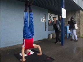 Tony Helou, 75, performs a headstand on Saturday, Oct. 16, 2021, in Deux-Montagnes north of Montreal, to earn the Guinness World Record for oldest person to do a headstand, the first ever record in this category. His daughter Rola Helou, right, shot video as her father held the headstand for about 50 seconds. Expert and professional witnesses gathered to attest.
