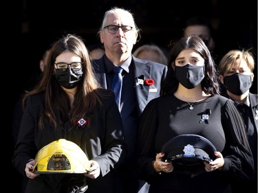The daughters of firefighter Pierre Lacroix, Stephanie and Annick, carry his helmet and dress cap as they leave his funeral at Notre-Dame Basilica on Friday, Oct. 29, 2021. Yves Lacroix, Pierre's brother, follows behind.