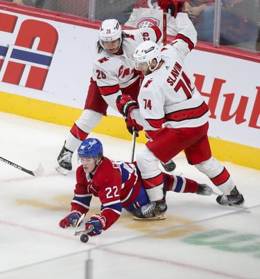 Montreal Canadiens' Cole Caufield plays the puck while falling down after being checked by Carolina Hurricanes Ethan Bear and Jaccob Slavin during second period at the Bell Centre Thursday, Oct.21, 2021.