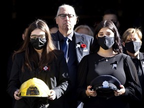 The daughters of fire fighter Pierre Lacroix, Stephanie and Annick ,carry his helmet and his dress cap as they leave his funeral at Notre-Dame Basilica Oct. 29, 2021. Yves Lacroix, Pierre's brother follows the girls.