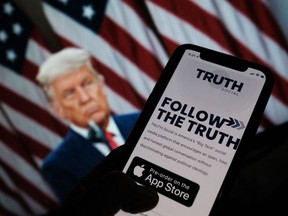 This illustration photo shows a person checking the app store on a smartphone for "Truth Social", with a photo of former US president Donald Trump on a computer screen in the background, in Los Angeles, Oct. 20, 2021.