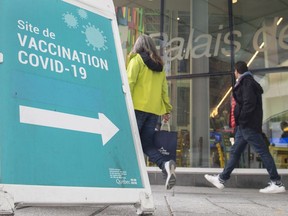 People walk by a sign advertising a COVID-19 vaccination site, in Montreal, Sunday, Oct. 3, 2021.