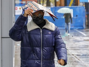 Jade Touré uses a shopping bag to keep the rain off her head while walking on Ste-Catherine St. in Montreal Oct. 31, 2021.