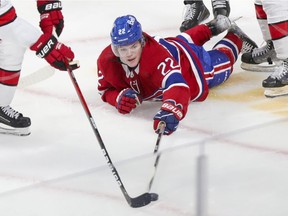 Montreal Canadiens' Cole Caufield pokes the puck away from Carolina Hurricanes' Derek Stepan while laying on the ice during second period in Montreal on Oct. 21, 2021.