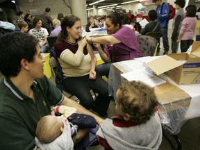 Nurse Faiza Alaoui administers an H1N1 vaccine to a woman as her family watches at a vaccination clinic at Olympic Stadium on Nov. 15, 2009.