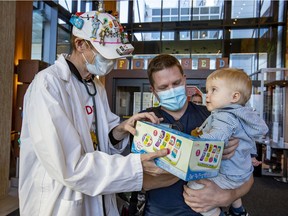 The Toy Doctor Norman Brown gives a gift to 14-month-old Renaud Deshaies, with his father Olivier at the Shriners Hospital for Children in Montreal Wednesday Nov. 24, 2021.
