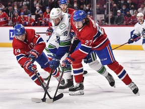 Jason Dickinson #18 of the Vancouver Canucks gets caught between Nick Suzuki #14 and Alexander Romanov #27 of the Montreal Canadiens during the first period at the Bell Centre on Nov. 29, 2021 in Montreal.