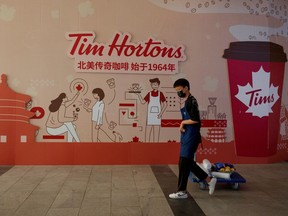 A man walks past a store front poster advertising the opening of a cafe of the Canadian coffee and fast food chain Tim Hortons in Beijing, China, July 6, 2020. Picture taken July 6, 2020.  REUTERS/Thomas Peter