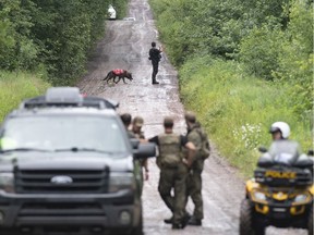 A K9 unit and police officers search a back road on Saturday, July 11, 2020 in Saint-Apollinaire, Quebec for two girls who were the subject of an Amber Alert.