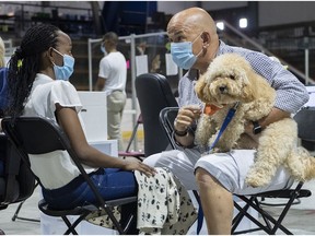 Zootherapist Sylvain Gonthier and dog Bidule comfort Divine Nsabimana as she waits to receive a COVID-19 vaccine at a clinic in Montreal on Aug. 26, 2021.