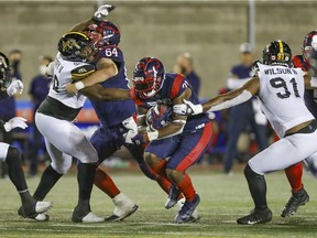 Montreal Alouettes tailback William Stanback hits a hole as offensive-lineman Sean Jamieson blocks Hamilton Tiger-Cats Lee Autry II, left, during game in Montreal on Aug. 27, 2021. Ticats' Eddy Wilson II reaches for the tackle.