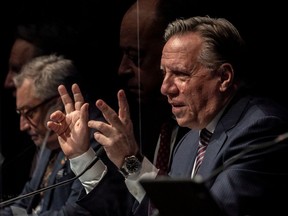 Quebec Premier François Legault, accompanied by public health director Horacio Arruda, with Health Minister Christian Dubé seen in reflection, during a COVID-19 press conference in Montreal on Wednesday December 22, 2021.