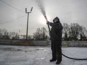 With the low rising winter sun in background, Montreal city worker Yves sprays water on a hockey rink at Beaubien Park on Monday Dec. 27, 2021.