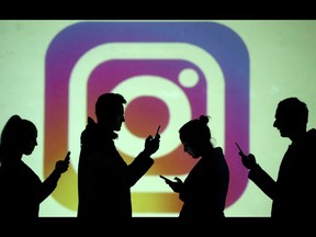 Silhouettes of mobile users are seen next to a screen projection of Instagram logo in this picture illustration taken March 28, 2018.