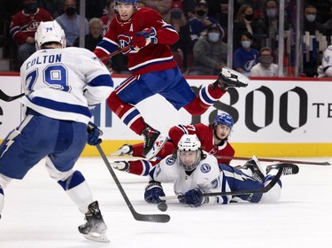 Montreal Canadiens centre Nick Suzuki (14) gets airborne as he jumps over Tampa Bay Lightning centre Anthony Cirelli (71) after Cirelli collided with Montreal Canadiens defenseman Alexander Romanov (27), rear, during second period in Montreal on Tuesday, Dec. 7, 2021. Tampa Bay Lightning left wing Ross Colton (79) recovers the puck on the play.