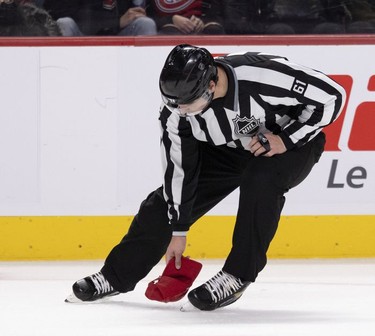 Linesman James Tobias picks up a hat thrown on the ice surface as the Montreal Canadiens throw away the lead against the Tampa Bay Lightning during third period in Montreal, on Tuesday, Dec. 7, 2021.