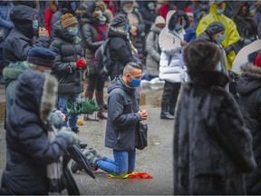 A man kneels during New Year's mass in the parking lot behind Mary Queen of the World Cathedral in Montreal Saturday January 1, 2022.
