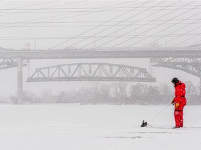 Charles Hu fishes in the St. Lawrence River under the shadow of the two Champlain Bridges in Brossard on Friday January 7, 2022. The centre span of the original bridge is lowered behind the new one.