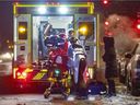Eine Frau beobachtet, wie Sanitäter am Mittwoch, den 12. Januar 2022, in Montreal einen COVID-Patienten in einen Krankenwagen laden.