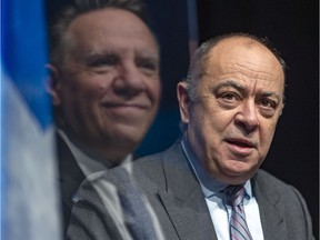 Premier François Legault is reflected in a plastic divider as he listens to Health Minister Christian Dubé during a press conference in Montreal in January 2022.