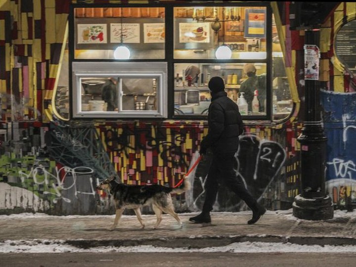  A man looks inside a restaurant as he walks a dog on Pins Ave. in Montreal after curfew on Friday, January 7, 2022.