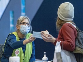 A woman is given a new procedural mask at the COVID-19 vaccination centre in the Palais des Congrés in Montreal on Thursday, Jan. 20, 2022..