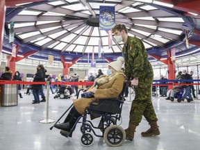 A member of the Canadian Armed Forces wheels a woman into a COVID-19 vaccination clinic at the Olympic Stadium in Montreal, on Thursday, January 6, 2022.
