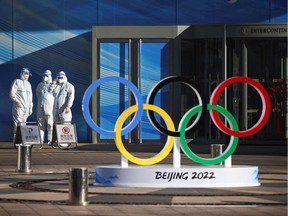 Workers in PPE on Dec. 30 stand next to the Olympic rings inside the closed loop area near the National Stadium, or the Bird's Nest, where the opening and closing ceremonies of Beijing 2022 Winter Olympics will be held, in Beijing, China.