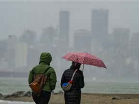 People walk in the rain along Spanish Banks as the city is hidden behind a wall of rain in Vancouver, Nov. 7, 2021.