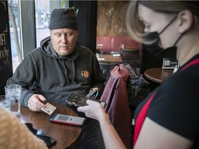 Dany Bolduc shows his vaccine passport and ID to waitress Brianna Holland while sitting with Alexadra Dubreuil-Gagnon at the Burgundy Lion last month. As of March 14, the passport will no longer be required in Quebec.