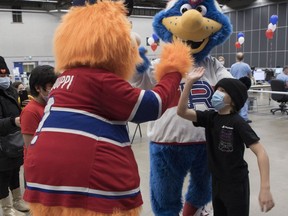 Kyle Appleby gets a high-five from Montreal Canadiens mascot Youppi! as Laval Rocket mascot Cosmo looks on, at the Palais des congrès Saturday, February 5, 2022. The CIUSSS du Centre-Sud-de-l'Île-de-Montréal paired up with the Montreal Canadiens to encourage vaccination among children in the city.