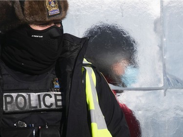 A person is seen through the Quebec Carnaval ice castle while Quebec police officers look at protesters in front of Quebec's National Assembly during a massive protest against COVID-19 vaccine and health restrictions on Saturday, Feb. 5, 2022.