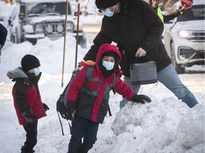 Father Russ Cooper hands out school bags to his sons, Evan, left, and Bruce, as they prepare for their back-to-school day in Montreal on Jan. 18, 2022.