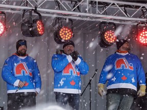 Protest organizers Bernard Gauthier, centre, Keven Bilodeau, left, and Kevin Grenier, right, are seen on a stage by the National Assembly in Quebec City on Saturday.