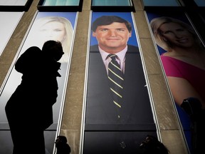 People pass by a promotional photo of Fox News host Tucker Carlson on the News Corporation building in New York.