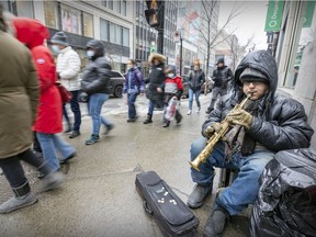 Busker Robin plays his saxaphone as pedestrians pass on Saint-Catherine St. at Peel in downtown Montreal Friday March 11, 2022.