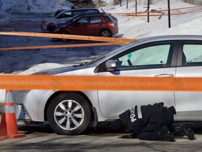 A Montreal police officer looks for evidence underneath a Toyota parked on Pierre-Corneille St. across from Place Versailles. A man was shot dead early March 10, 2022.