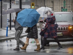 Pedestrians shelter under umbrellas while crossing Peel St. on a rainy day in Montreal.