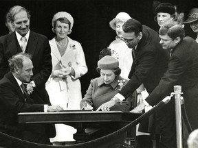 Seated with the Queen is Prime Minister Pierre Trudeau. Assisting at the table are Michael Pitfield (wearing glasses) and Michael Kirby, respectively secretary to the cabinet and associate cabinet secretary.