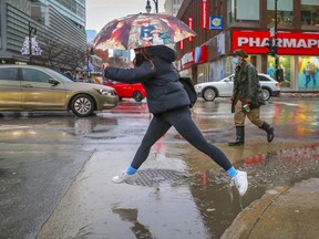 A woman jumps a puddle at the corner of Ste-Catherine and Guy St. in 2021.