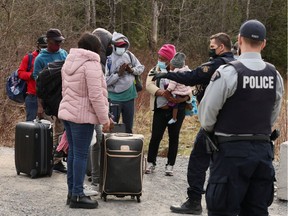 Asylum seekers talk to a police officer as they cross into Canada from the U.S. near a checkpoint on Roxham Rd. near Hemmingford, Que., on April 24, 2022.