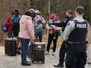 Des demandeurs d'asile parlent à un policier alors qu'ils entrent au Canada depuis les États-Unis près d'un point de contrôle sur Roxham Rd. près de Hemmingford, au Québec, le 24 avril 2022.