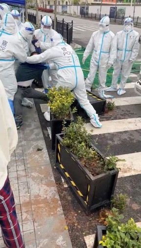 Police officers wearing hazmat suits detain a man, as residents protest over neighbouring residential compounds being turned into COVID-19 isolation facilities, in Pudong, Shanghai, China, in this screen grab from a video reported to be April 14, 2022.