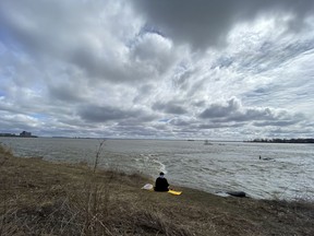 A woman sits along on the shore of the St. Lawrence River in the Verdun district of Montreal, on Wednesday, April 1, 2020. "If passed, the bills would create a system of guardians responsible for protecting the St. Lawrence’s rights, including through legal procedures when necessary," Elara Neath Thomin writes.