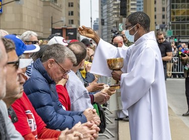 A priest administers holy communion to fans outside the funeral for Guy Lafleur at Mary Queen of the World Cathedral in Montreal Tuesday, May 3, 2022.
