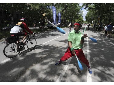 Hamza Araqi juggles near Lafontaine Park as people ride by during the Tour de l'Île in Montreal on Sunday, June 5, 2022.