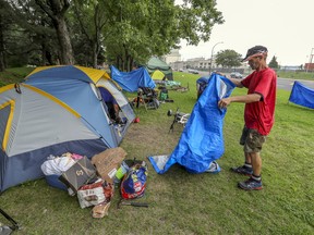 An unhoused man folds a tarp outside his tent at an encampment along Notre-Dame St. East in Montreal Sunday August 9, 2020.