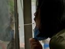 A health worker  reaches out of a window to take a swab sample from a woman to be tested for COVID-19 in Beijing on June 9, 2022.
